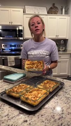 a woman holding two trays of food on top of a kitchen counter next to an oven