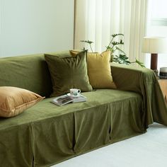 a green couch with some pillows on it and a book in front of the couch