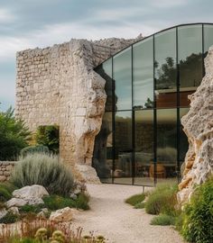 a building made out of rocks with glass windows on the front and side walls, surrounded by greenery