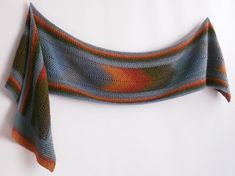 a crocheted shawl draped over a white wall with an orange, blue and green design