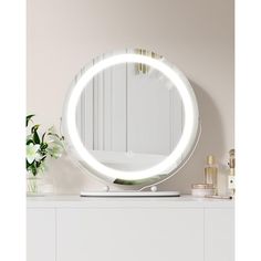 a round mirror sitting on top of a white dresser next to a vase with flowers