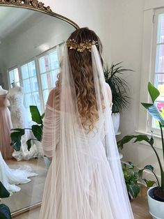 the back of a bride's wedding dress in front of a mirror with her veil pulled back