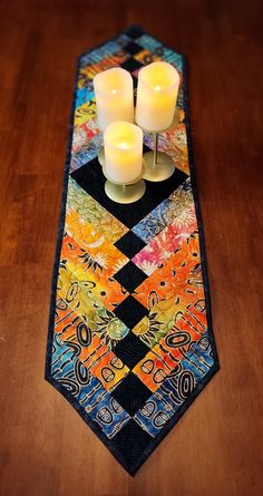 two candles are placed on top of a colorful neck tie with an intricate design and diamond pattern