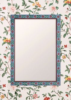 an ornate blue frame with flowers and leaves on the wall behind it is a mirror