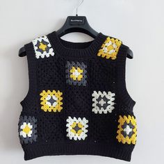 a black sweater with yellow, white and gray flowers on it hanging from a hanger