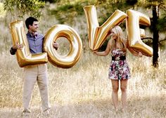 a man and woman holding gold balloons that spell out love in the middle of a field