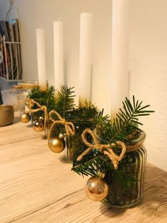 candles are lined up on a table with evergreen branches and ornaments in them, along with pine cones