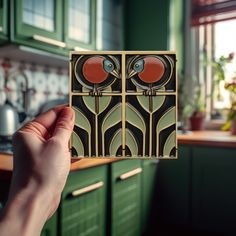 a hand holding up a piece of art deco tile in a kitchen with green cabinets