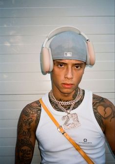 a man with headphones on his ears and wearing a white tank top is standing in front of a wall