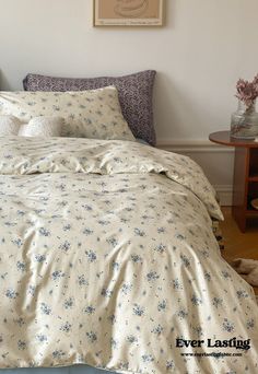 a bed with white sheets and blue flowers on it in a room next to a table