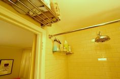 a bathroom with yellow tiled walls and white tile flooring, including a towel rack above the shower head