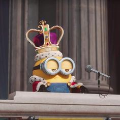 a minion with a crown on his head is standing in front of a microphone