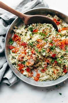 a pan filled with rice and vegetables on top of a table next to a wooden spoon