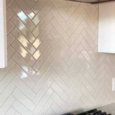 a stove top oven sitting next to a white kitchen wall with chevron tiles on it