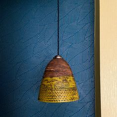 a yellow and brown lamp hanging from a wall next to a blue patterned wallpaper