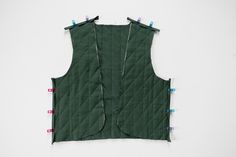 a green quilted vest hanging on a wall with clothes pins attached to the back