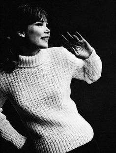 a black and white photo of a woman with her hands in the air while wearing a sweater