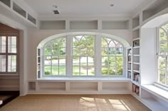 an empty living room with large windows and white furniture in the center, along with built - in bookshelves