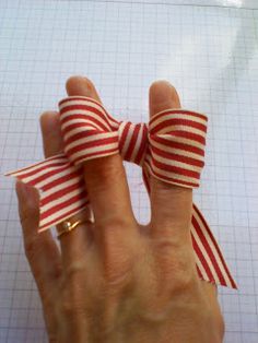 a hand with a red and white striped bow on it's finger, next to a piece of graph paper