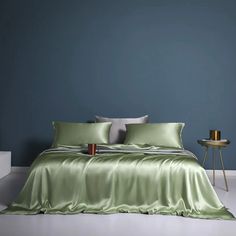 a bed with green sheets and pillows against a blue wall, next to a side table