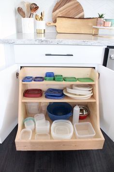 an open cabinet in the kitchen with dishes and utensils sitting on it's bottom shelf