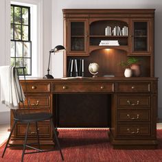 a wooden desk sitting in front of a window next to a chair and bookshelf