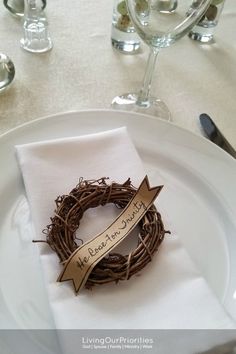 a white plate topped with a grapevine wreath next to wine glasses and silverware