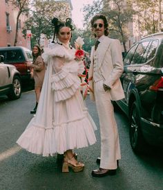 a man and woman dressed in wedding attire standing next to each other on the street