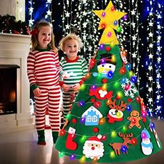 two children in pajamas standing next to a christmas tree with lights and decorations on it