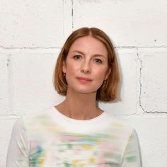 a woman standing in front of a white brick wall with her head tilted to the side