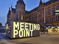 a large sign that says meeting point on the side of a road in front of some buildings