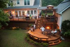 people are sitting on the back deck of a house at night with their lights on