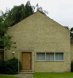 a brick house with a wooden door and window on the front lawn, next to a tree