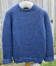 a blue sweater sitting on top of a wooden stand in front of a wood fence