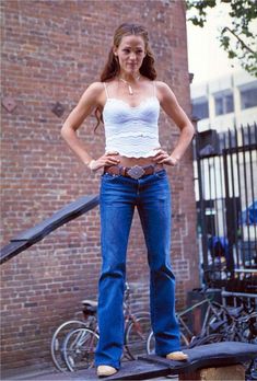 a woman standing on top of a skateboard in front of a brick building with her hands on her hips