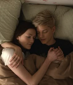 a man and woman laying in bed with their arms wrapped around each other's shoulders