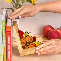 a person is holding an object in front of some books on a table with sunflowers