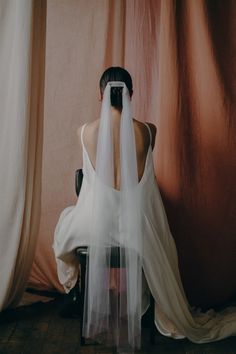 the back of a woman's head with a veil over her face sitting on a chair