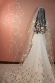 the back of a bride's wedding dress with flowers on it and a veil over her head