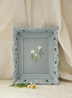 two daisies in a blue frame on a white background with some flowers laying next to it