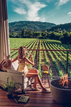 a woman sitting on top of a chair next to a fire pit in front of a vineyard