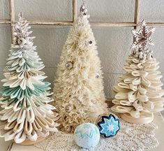 three ceramic christmas trees sitting on top of a doily covered table next to an egg