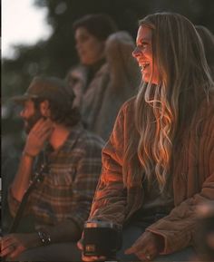 a group of people sitting next to each other on top of a field at sunset