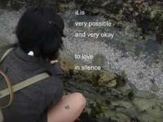 a woman sitting on the ground with her back to the camera, looking at water