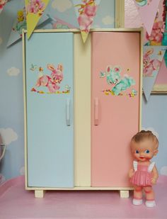 a doll standing next to a toy refrigerator in a room with decorations on the walls