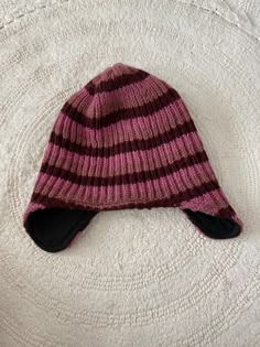 a pink and black striped hat laying on top of a white bed sheet with the bottom part of it's cap pulled back