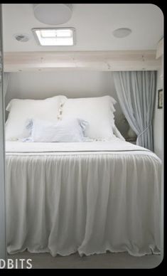 there is a bed with white sheets and pillows in the room that has blue curtains