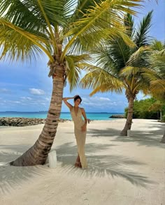 a woman standing under a palm tree on the beach