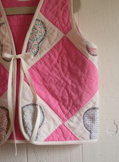 a pink and white quilted vest hanging on a wall