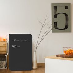 a black refrigerator sitting on top of a wooden floor next to a vase filled with oranges